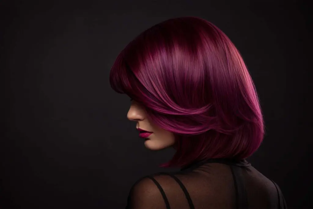 Profile view of a person with a layered bob in a vivid hair color, styled in vibrant magenta to match their lipstick.