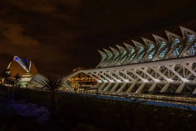 The City of Arts and Sciences in Valencia at night, featuring a long, arched structure with white structural ribs and a domed building in the background.