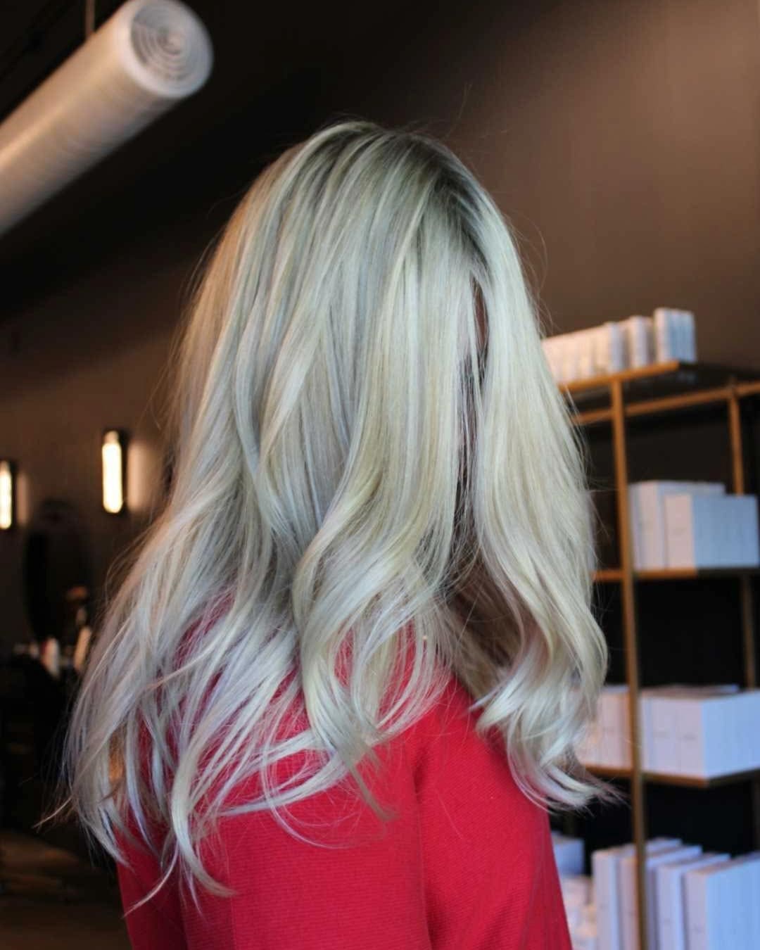 A person with long, wavy blonde hair facing away, wearing a red top. The background features shelves with white boxes and dark walls, creating a modern and stylish setting.