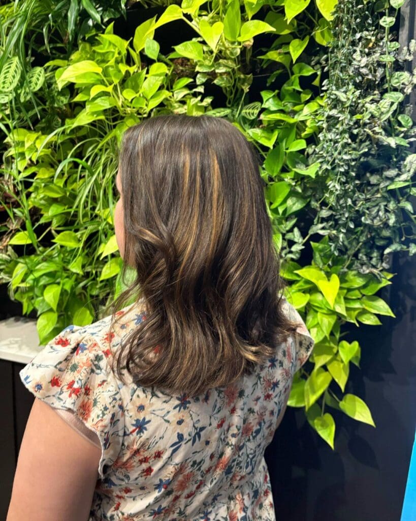 A client at Sunday Salon in Raleigh showcasing a bouncy shoulder-length style with a deep chocolate brown base and warm caramel ribbon highlights.