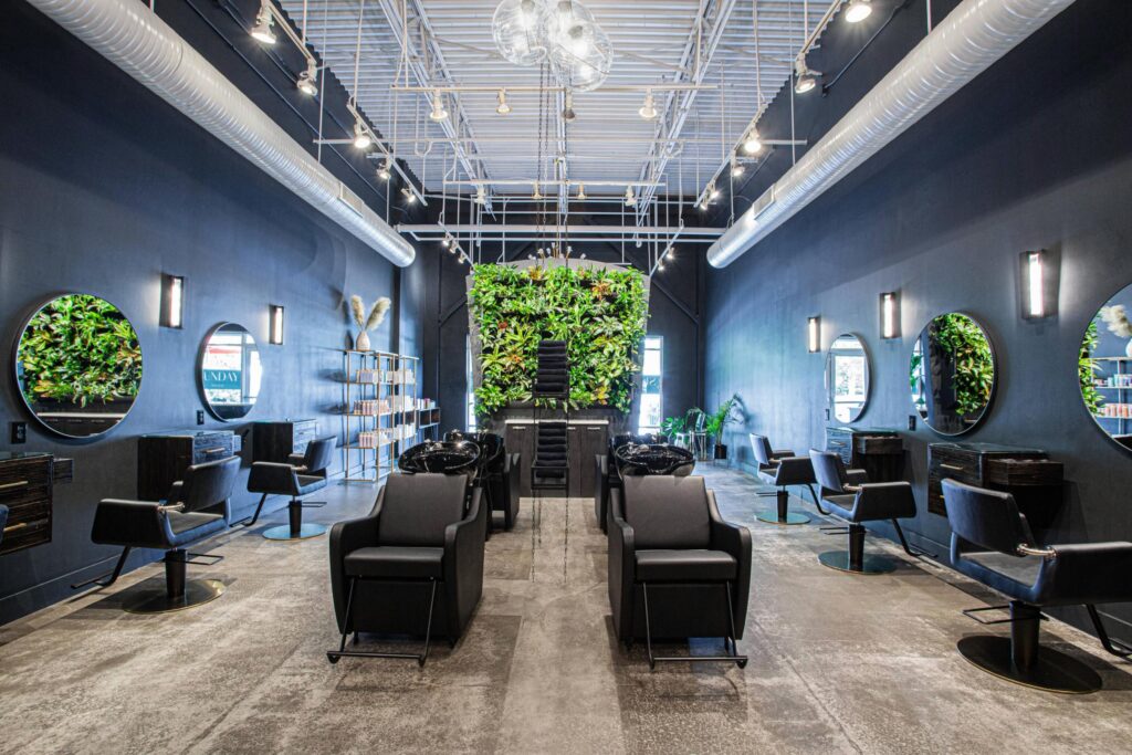 Modern, award winning salon with black chairs, round mirrors, and wall-mounted plants. The space features high ceilings, exposed ducts, bright lighting, and a large green plant wall at the back for a stylish, inviting atmosphere.