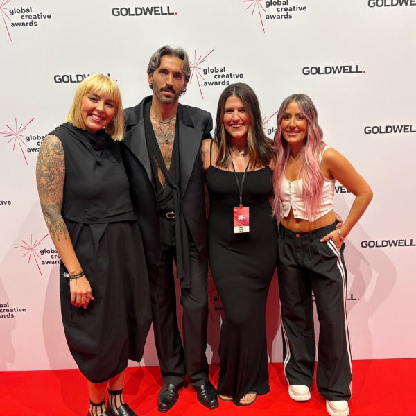 Four people pose together on a red carpet at the Global Creative Awards event, standing in front of a white backdrop with event logos. They are dressed in fashionable, semi-formal and casual clothing, smiling at the camera.