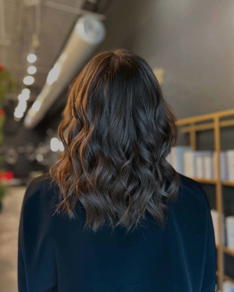A client with a mid-length dark chocolate brunette lob styled in a voluminous blowout with bouncy, defined waves and incredible shine at Sunday Salon in Raleigh.