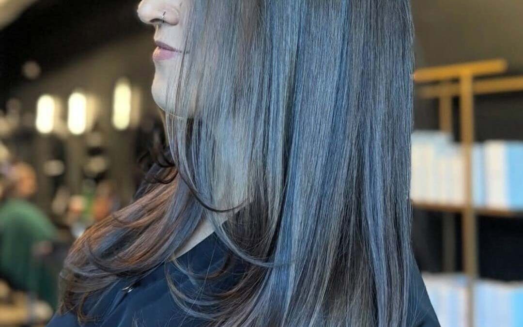 A side profile of a client with long, sleek dark cool-toned brunette hair featuring smooth face-framing layers and gently beveled ends, styled at Sunday Salon in Raleigh.
