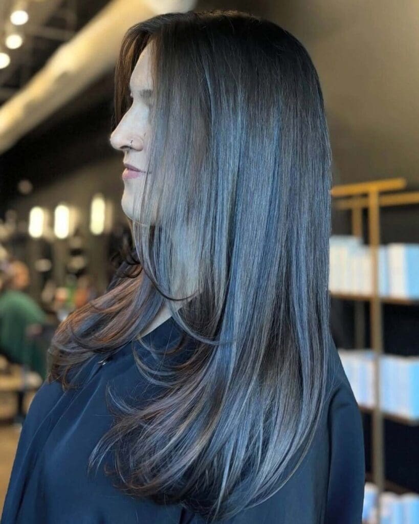 A side profile of a client with long, sleek dark cool-toned brunette hair featuring smooth face-framing layers and gently beveled ends, styled at Sunday Salon in Raleigh.