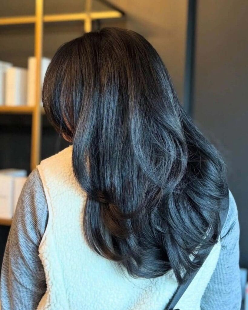 A client with long, thick, dark espresso brunette hair styled in a highly voluminous blowout with bouncy layered ends, crafted at Sunday Salon in Raleigh.