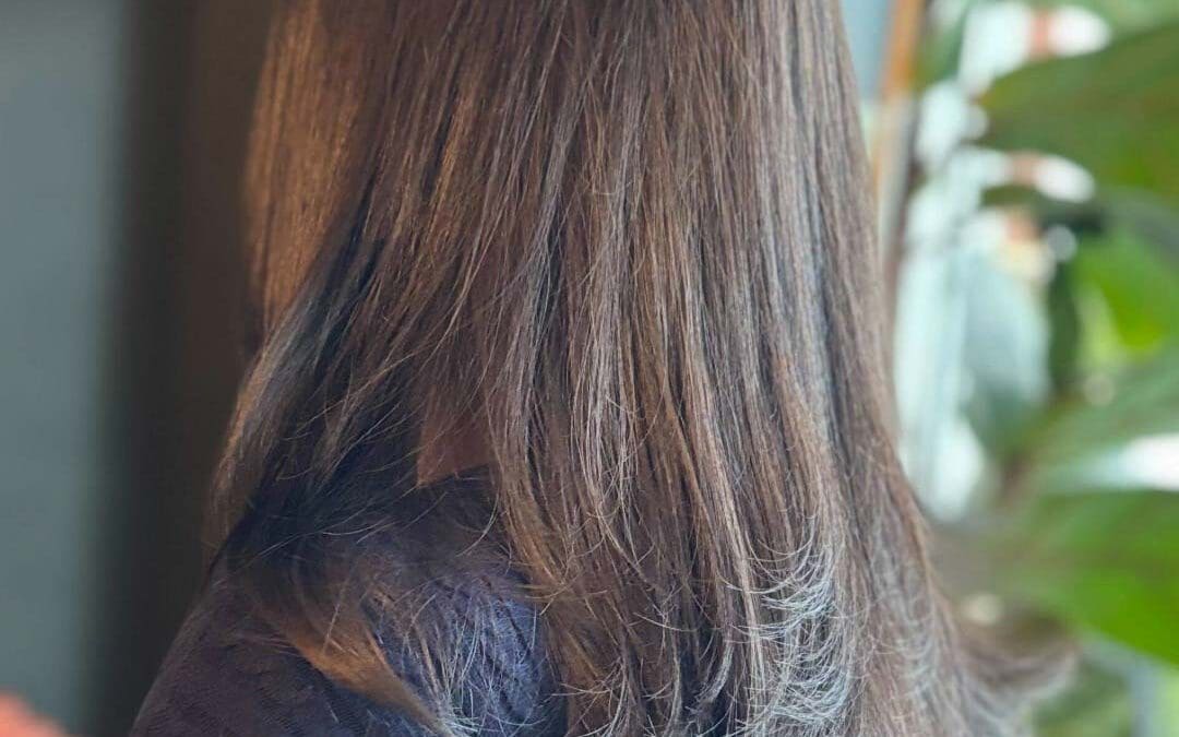 A client showcasing mid-length soft dark brunette hair styled in a sleek blowout with gently flipped textured ends, beautifully crafted at Sunday Salon in Raleigh.