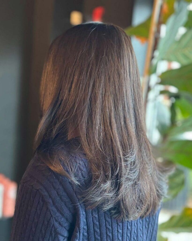 A client showcasing mid-length soft dark brunette hair styled in a sleek blowout with gently flipped textured ends, beautifully crafted at Sunday Salon in Raleigh.