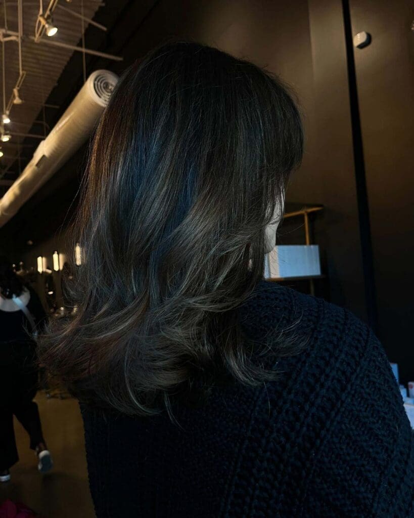 A client showcasing a sophisticated mid-length deep espresso brunette haircut styled with a smooth blowout and sweeping layered ends at Sunday Salon in Raleigh.